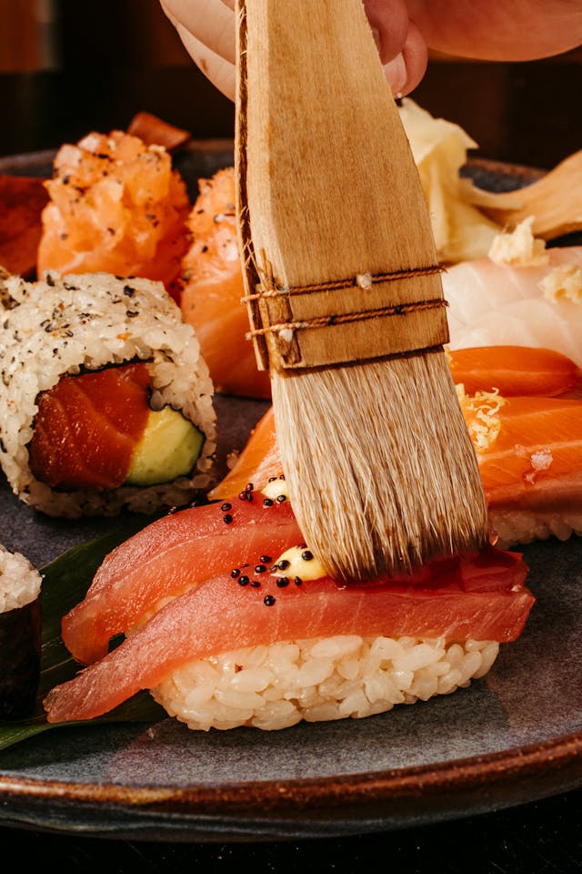 A brush adding some sauce to a tuna nigiri.